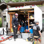 Three people clean up gear and put it back into the equipment van.