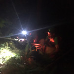 Dr. Jeff Dahl crests the edge of the cliff with Bella the dog in his arms. Night time photo of someone holding a dog at the edge of a cliff.