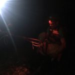 Dr. Jeff Dahl crests the edge of the cliff with Bella the dog in his arms. Night time photo of someone holding a dog at the edge of a cliff.